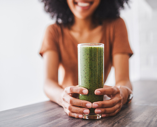 Afro smiling woman with hands around a glass of an healthy green detox beverage