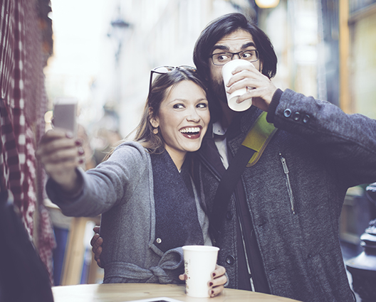 Happy and smiling couple taking selfie at coffee shop table in streets