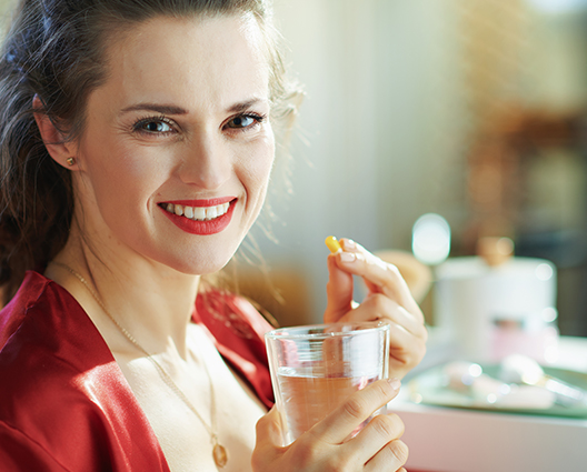 Smiling woman holding capsule and glass of water