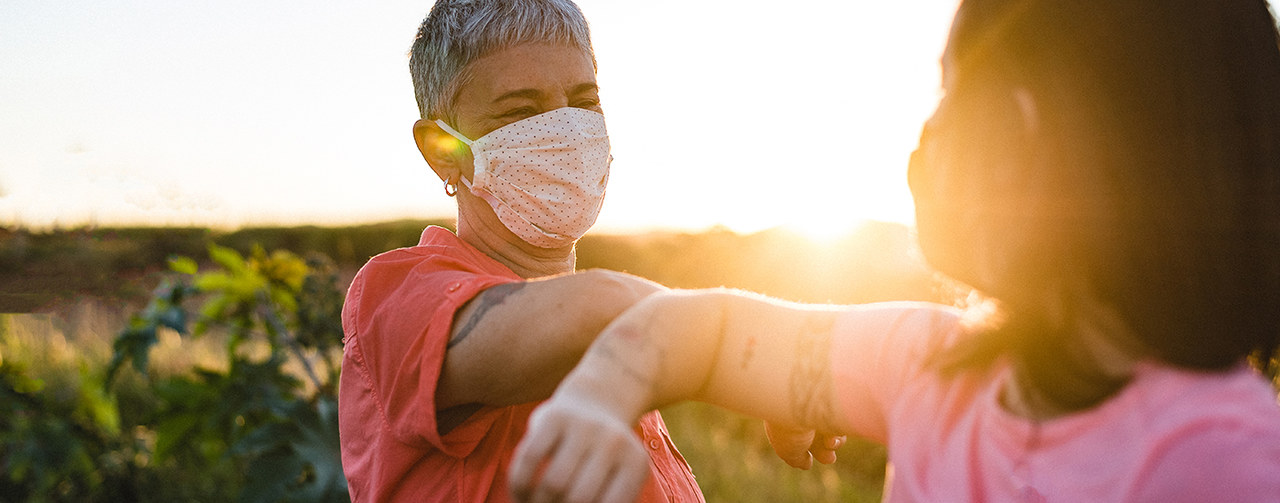 Happy women wearing protective mask in elbow salute