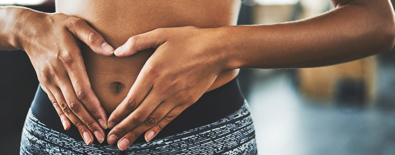 Woman making a heart shaped gesture over her stomach in a gym