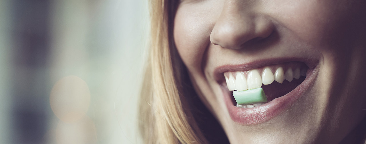 Happy woman holding chewing gum with her teeth