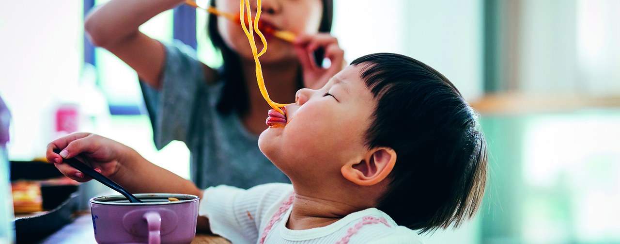 Asian little girls eating noodles at home