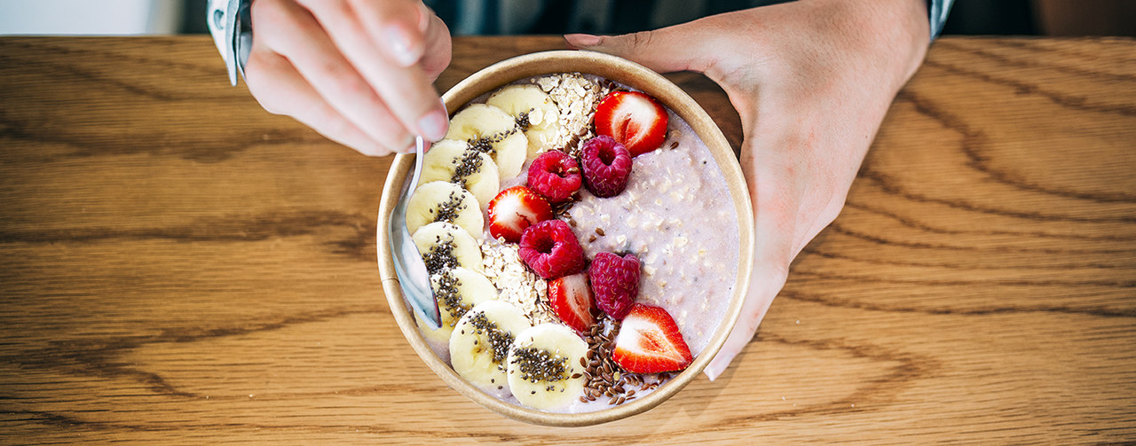 Crop woman close up eating oat and fruits bowl for breakfast