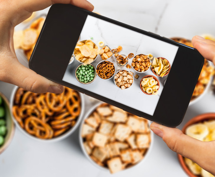 Close up of hands holding smartphone and taking a picture of a snacking table