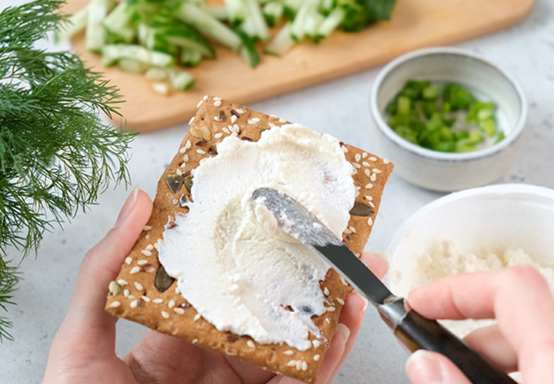 Hand spreading cream cheese with knife on cracker