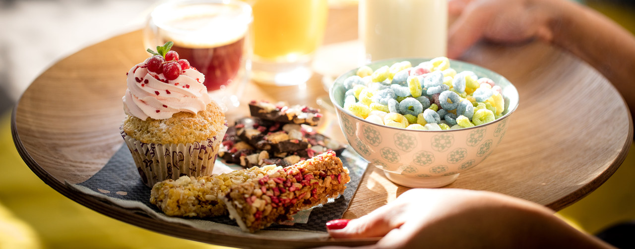 Woman's hands holding a tray with an assortment of bakery and cereals