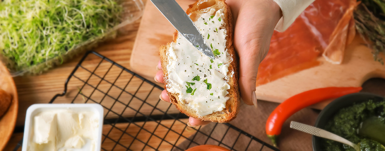 Hand spreading cream cheese with knife on bread