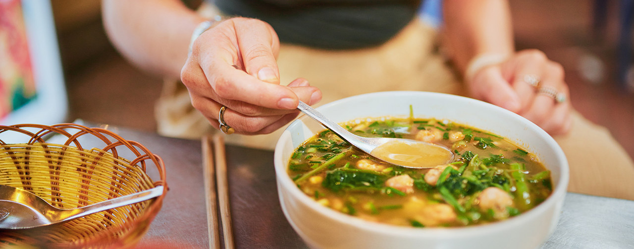 Woman eating soup broth on wooden table