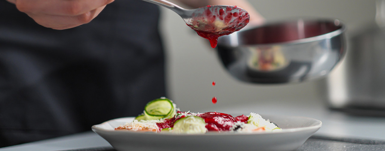 Woman chef pouring red sauce on meal