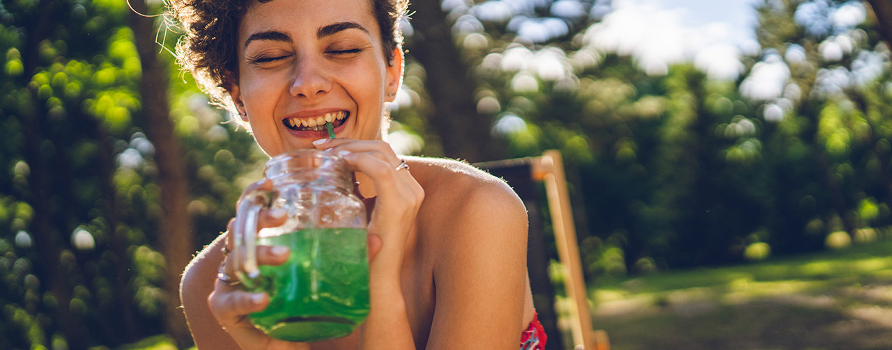 Smiling woman drinking green instant drink in a jar