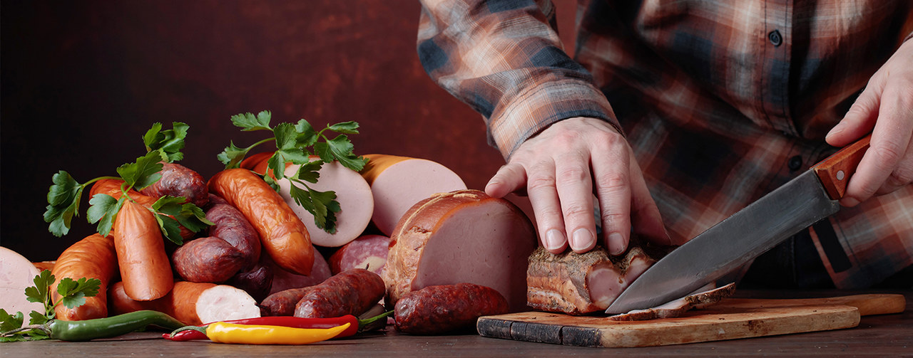 Man cuts various sausages and smoked meat