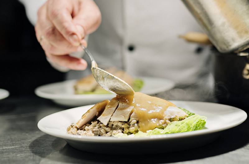 chef's hand pouring sauce on a meat dish