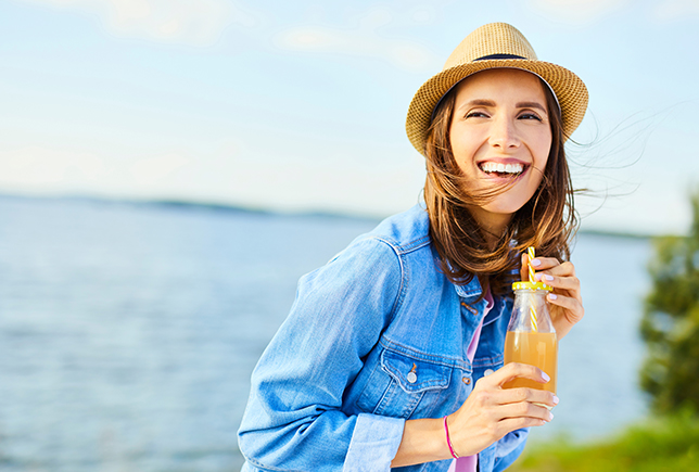 Smiling woman drinking a drink near the water