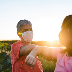 Happy women wearing protective mask in elbow salute