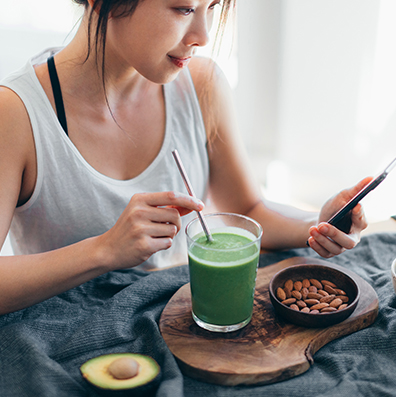 Asian woman using smart phone while drinking green smoothie