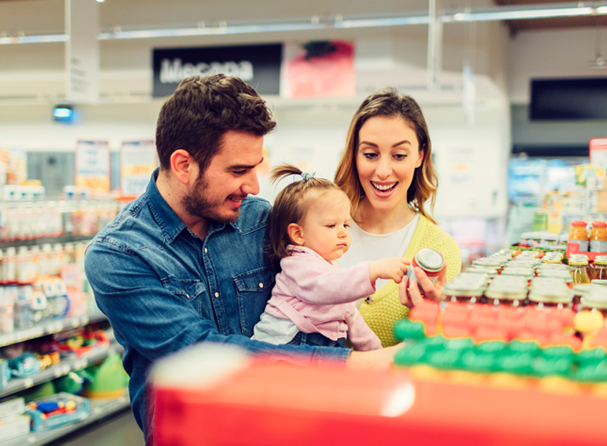 Happy parents with their child choosing baby food products in supermarket