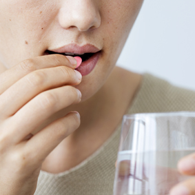 close up of woman taking red pill with a glass of water