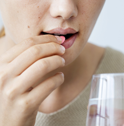 close up of woman taking red pill with a glass of water