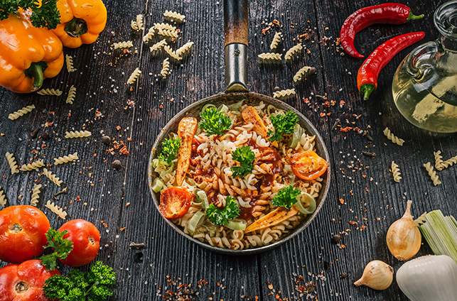 Fusilli and vegetables in a pan on dark wooden table