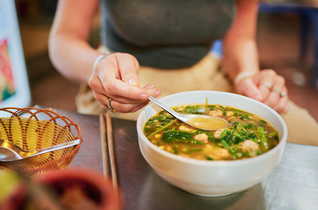 Woman eating soup broth on wooden table