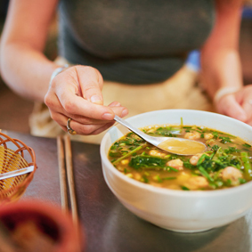 Woman eating soup broth on wooden table