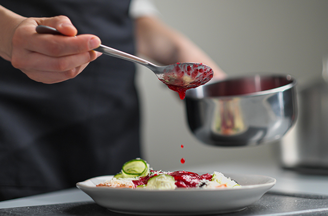 Woman chef pouring red sauce on meal