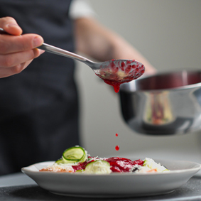 Woman chef pouring red sauce on meal