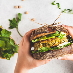 Vegan sandwich with chickpea patty, avocado, cucumber and greens in hands