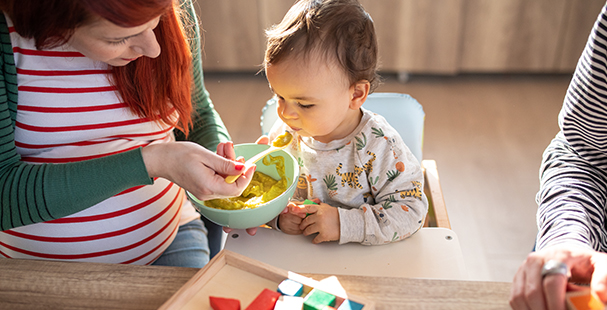 Pregnant woman feeding her baby boy with vegetable meat and fish mash at dinning room