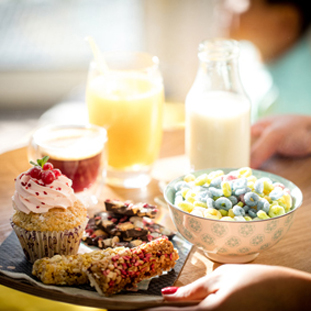 Woman's hands holding a tray with an assortment of bakery and cereals