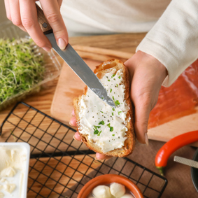 Hand spreading cream cheese with knife on bread