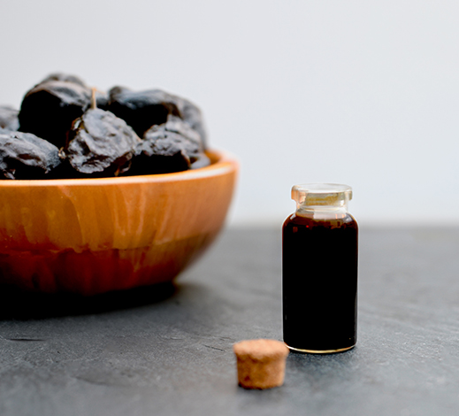 Prune juice concentrate in glass bottle and raw prunes in wooden bowl