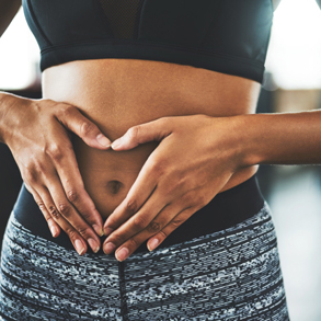 Cropped shot of a fit young woman making a heart shaped gesture over her stomach in a gym